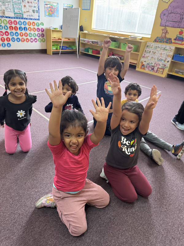 Children raising hands with excitement in classroom at Adventure Montessori Academy
